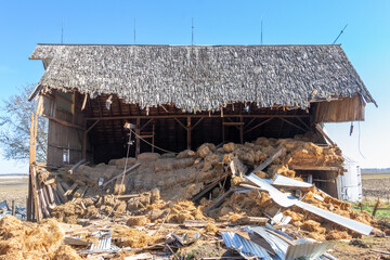 Close up view of an old abandoned barn building being demolished with a heavy equipment excavator