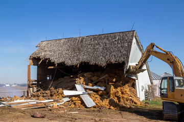 Close up view of an old abandoned barn building being demolished with a heavy equipment excavator
