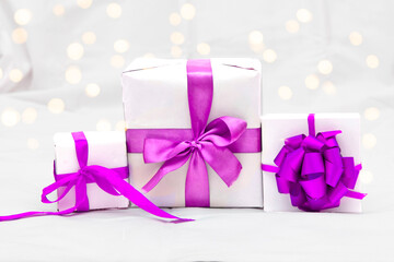 Decorative three white gift box with a large purple bow against a background bokeh of lights