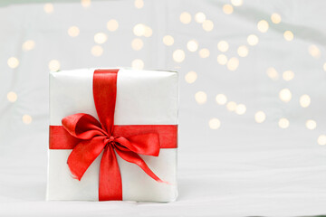 Decorative white gift box with a large red bow against a background bokeh of lights