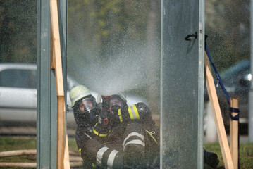 Two firefighters train the protective techniques with a jet pipe when igniting smoke gases at an apartment door