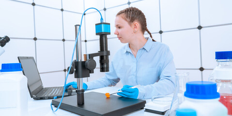 young woman laboratory assistant examines a sample of a mineral under a microscope in a mineralogy...