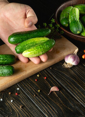The cook sorts cucumbers before canning in a jar. Work environment on kitchen table with vegetables and spices