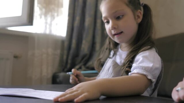 Cute smart preschool 5 years old girl writing homework in exercise copybook, learning letters, sitting at home table. Preparation for school. Home distance education. Children preschool concept.