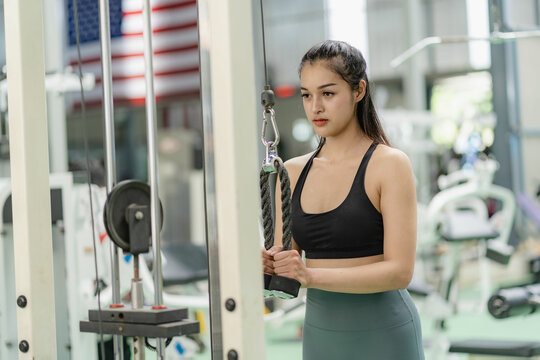 weight training Asian woman exercising in fitness gym, lifting weights, strong body, in sportswear, health care motivation concept, smiling at the gym.
