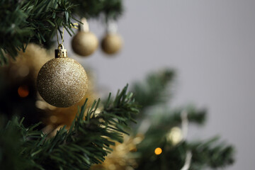 Closeup of a green Christmas tree with gold, white and silver ornaments, golden tinsel plus small decorative lights. Grey background. Joyful and happy holiday season color image. Merry xmas!