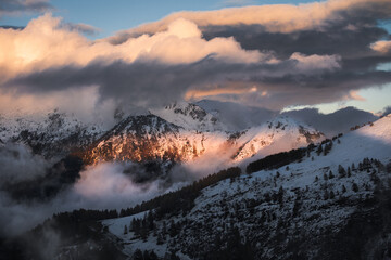 Low altitude clouds surround a snow covered mountain during sunset, Northern Italy,