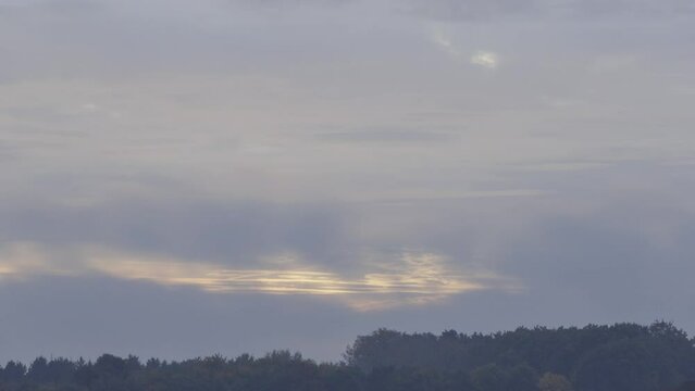 Time lapse shot of the rising sun shining through heavy clouds above a forest in autumn