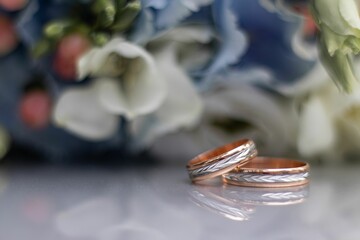 Closeup shot of two silver and copper wedding rings near a bouquet