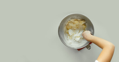 Children's hand mixing ingredients in a metal bowl for a homemade pastry. Flat lay. White background