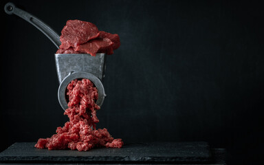 Making minced meat for beef meatballs in a manual meat grinder on a black background. Macro shot....