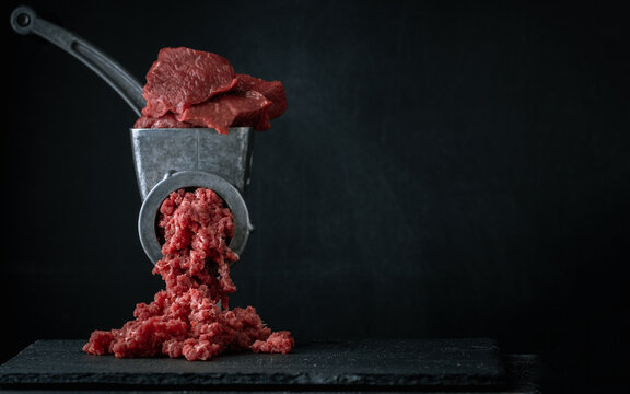 Making minced meat for beef meatballs in a manual meat grinder on a black background. Macro shot. Close up of metal meat grinder with raw meat
