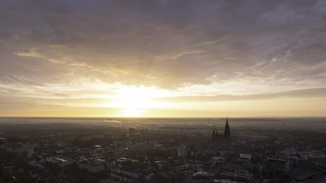 Aerial time lapse shot of Ulm city center with rising sun on a morning in autumn with colorful clouds moving through the sky