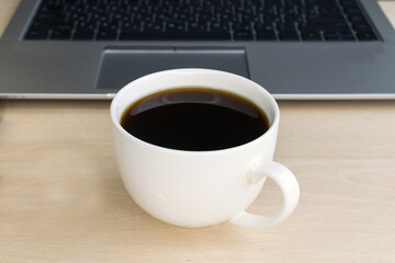 A cup of coffee on the background of a laptop computer. Morning. Work online. Break. Webinar
