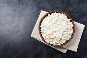 Cottage curd cheese in a wooden bowl on dark black table.