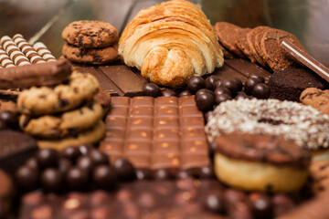 Freshly croissant with chocolate filling and variation of chocolates and cookies on rustic background