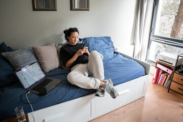 Asian brunette woman using her smartphone while sitting at the sofa alone