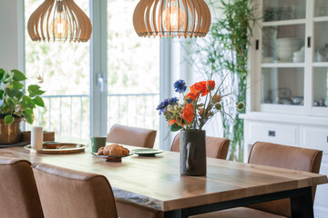 Wooden kitchen table with flowers in vase in a fancy bright kitchen