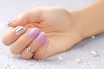 Close up womans hand with matte lavender nail design on gray furry background