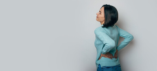 Spinal cord problems on woman's back. Chronic back pain. Young brunette woman is holding her lower...