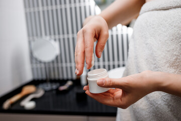 Close up of female hands taking moisturizing cream from bottle in bathroom. Woman taking care of her dry complexion