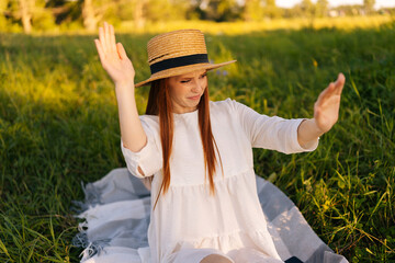 Portrait of dissatisfied redhead pretty woman in straw hat and white dress chasing insects away...
