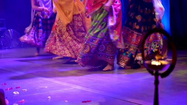 Low angle shot of unidentified girls legs in traditional ghagra dress dancing to Indian classical music in front of a diya or candle, India dance, festival and celebration concept