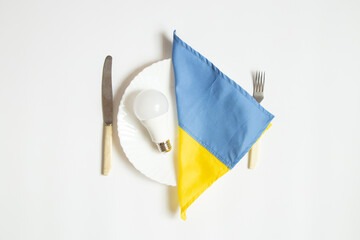 LED light bulb and the flag of Ukraine lie on a dinner plate and next to a knife with a fork on a...