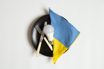LED light bulb and the flag of Ukraine lie on a dinner plate and next to a knife with a fork on a...