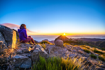 Sitting woman watching the sunrise over the beautiful mountain landscape of Pico do Ariero. Pico do...