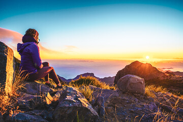 Naklejka premium Sitting woman watching the sunrise over the beautiful mountain landscape of Pico do Ariero. Pico do Arieiro, Madeira Island, Portugal, Europe.