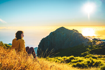 Woman sitting on a mountain meadow enjoying the beautiful mountain landscape of Pico do Ariero at...