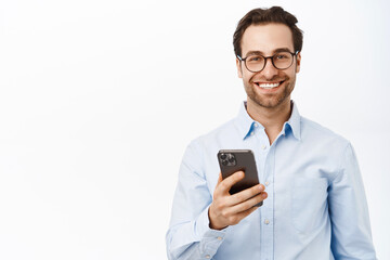 Handsome male entrepreneur using mobile phone, standing in glasses and blue shirt over white background - 543738111