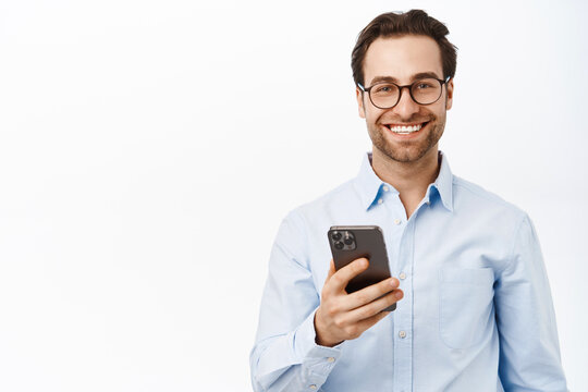Handsome male entrepreneur using mobile phone, standing in glasses and blue shirt over white background