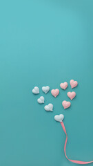 ten small meringues of pink and blue hearts are laid out in big heart with pink fabric ribbon on...