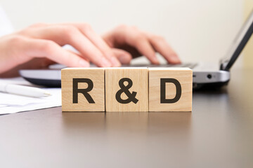 r and d - acronym from wooden blocks with letters. background hands on a laptop with blur. business concept. - obrazy, fototapety, plakaty