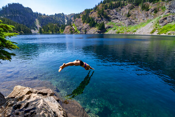 Adventurous athletic female hiker diving into an alpine lake in the Pacific Northwest.
