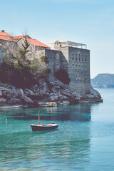 Small fishing boat on the Adriatic sea near Sveti Stefan Island, Montenegro. Turquiose water, islet with historical buildings. Mountains in the background. Fishing concept. Vertical photo