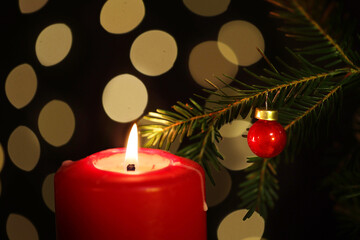 Lit red candle stands before yellow lights near green christmas tree branch