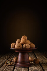 a pile of whole dried walnuts in a clay bowl against a brown backdrop with a vignette on a table made of old boards. moody vertical still life with copy space