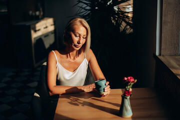 Thoughtful mature woman sitting in cafeteria holding coffee mug while looking away. Middle aged woman drinking tea or coffee while thinking.