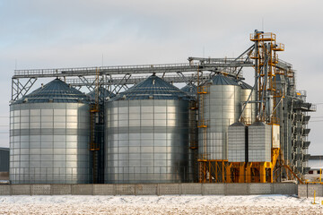 Silver silos against the blue sky in winter. Grain storage in winter at low temperatures. Production for processing, drying, cleaning and storage of agricultural products, flour, cereals and grain © Pokoman