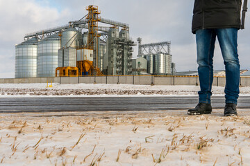 Silver silos in winter, wheat field covered with snow. The head of the agro-industrial complex stands near the plant for processing, drying, cleaning and storage of agricultural products, flour © Pokoman