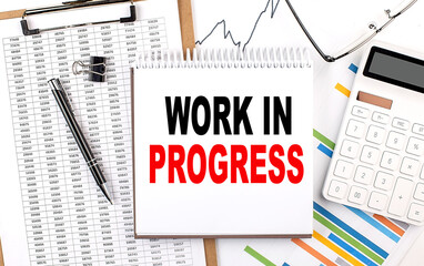 WORK IN PROGRESS text on notebook with chart, calculator and pen