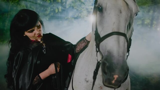 A fantasy medieval girl sorceress soothes a horse by stroking its mane while standing in a foggy fantasy forest at night. The horse is worried. 