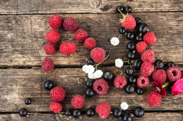 Ripe, juicy red raspberries and black currants are beautifully scattered on wooden boards.