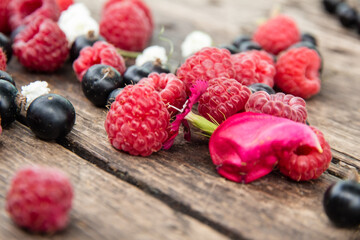 Ripe, juicy red raspberries and black currants are beautifully scattered on wooden boards.