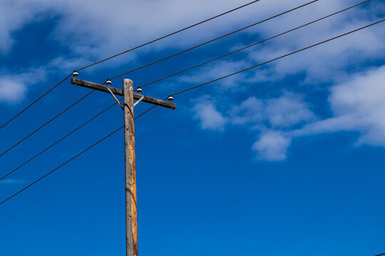 Utility pole and electrical wires against a blue sky with clouds. 
