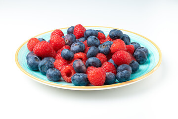 sky blue plate filled with black raspberries and blueberries on a white background