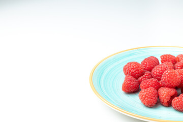 sky blue plate full of raspberries on white background